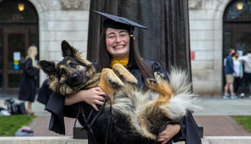 Student in grad cap and gown holding their dog