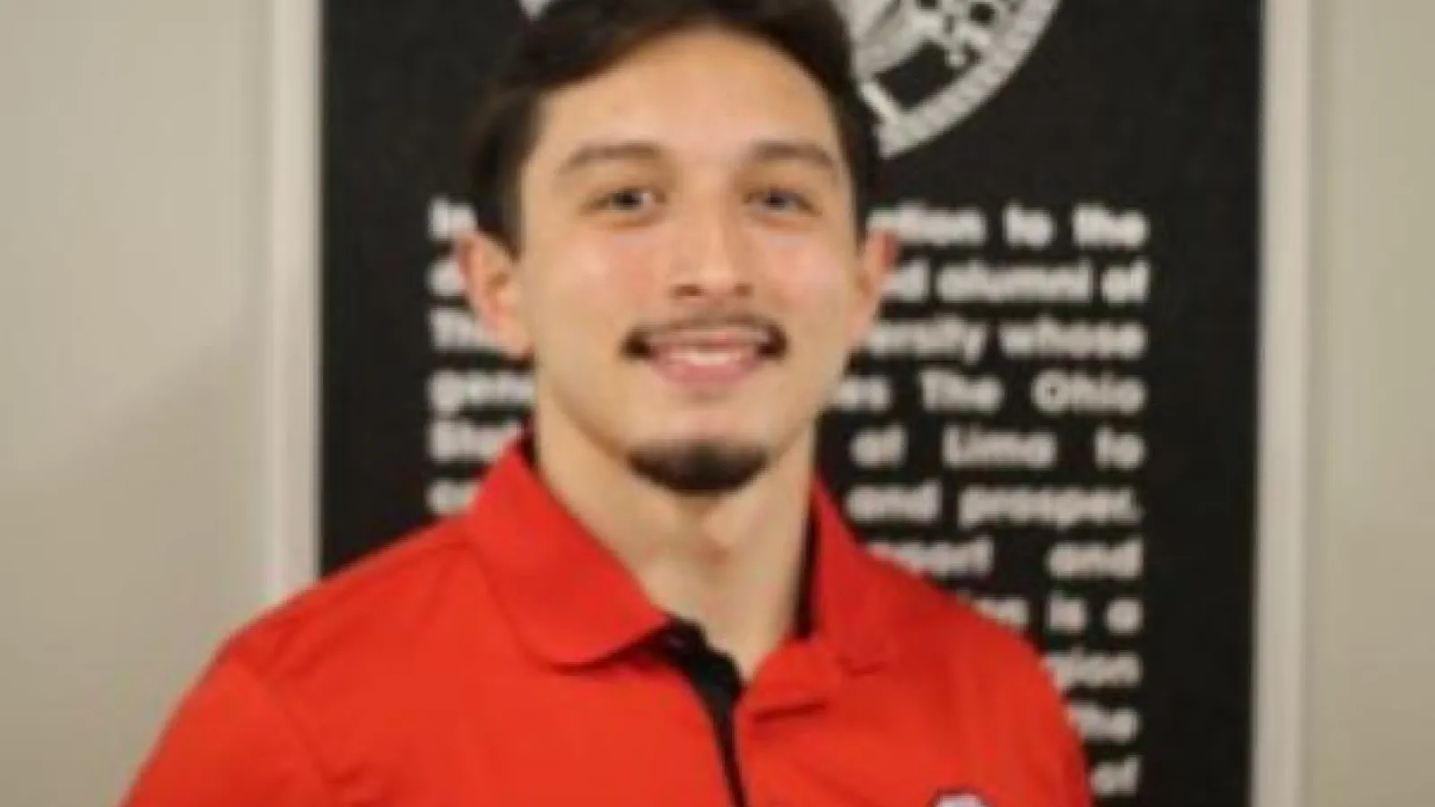 Student Ely Roa wearing a red polo shirt in front of black signage.