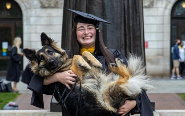 Student in grad cap and gown holding their dog