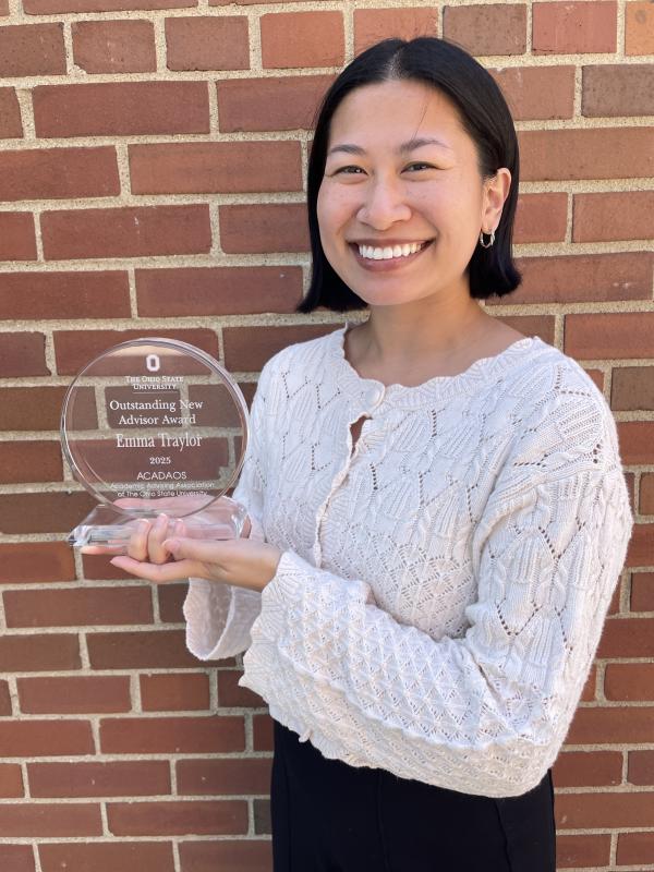 Photo of Emma in front of a brick wall holding an award.